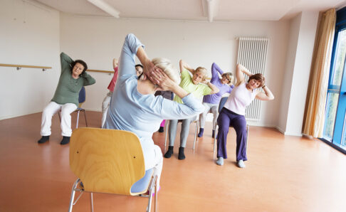 teacher and active senior women yoga class on chairs